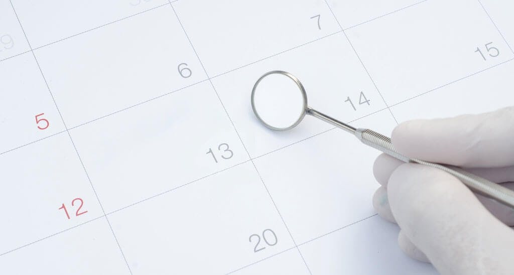 Zahnarzt zeigt mit Spiegel auf Datum auf Kalender