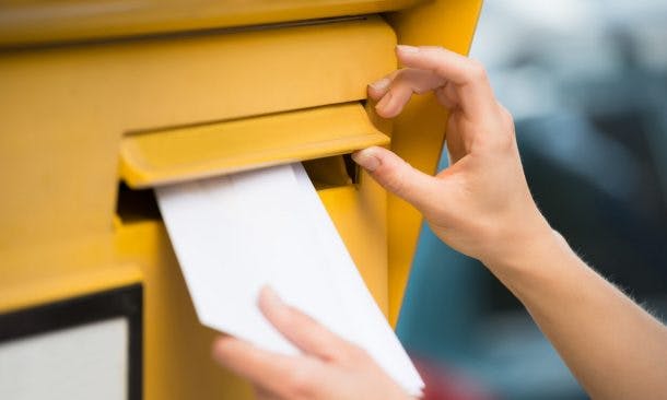 weibliche Hand wirft Brief in Postkasten ein